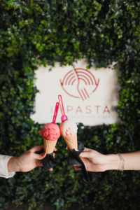 Two People showing the Ice cream cones they got at the Inpasta restaurant, with the logo behind them