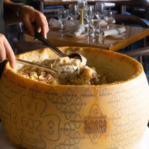 alt="a person spooning pasta into a cheesewheel in allegro restaurant"
