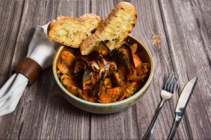 alt="a bowl filled with mussels and bread on top of a wooden table"